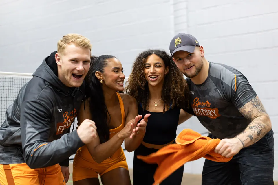 Vier Mitglieder der SportsFactory jubeln in orangefarbenen Team-Shirts